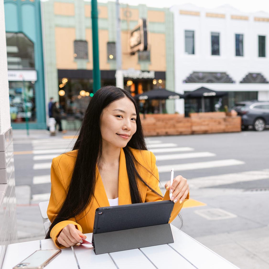 A young woman considers debt management plan pros and cons while sitting with a laptop at an outdoor cafe